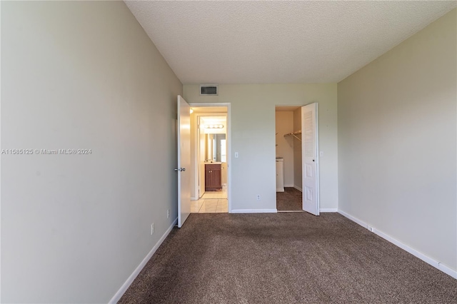 unfurnished bedroom with tile flooring, a closet, a walk in closet, and a textured ceiling