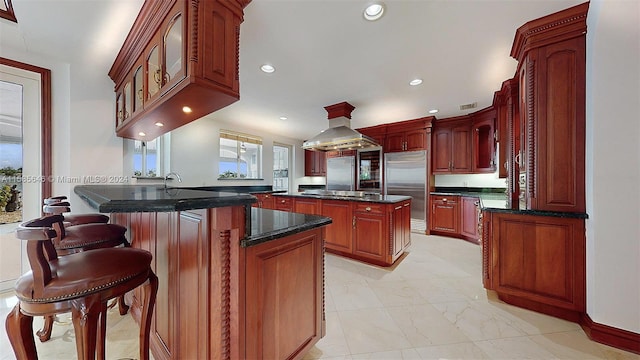 kitchen with light tile flooring, island range hood, built in fridge, black electric cooktop, and a center island