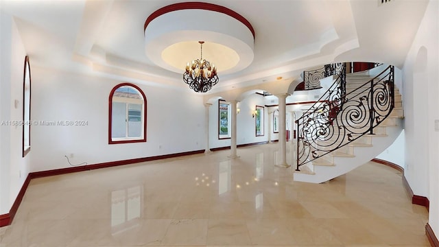 entryway featuring a tray ceiling, decorative columns, light tile floors, and an inviting chandelier