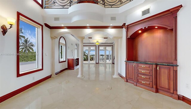 hallway with a towering ceiling, ornamental molding, decorative columns, and light tile floors