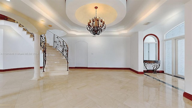 tiled entrance foyer featuring a notable chandelier, ornate columns, and a raised ceiling