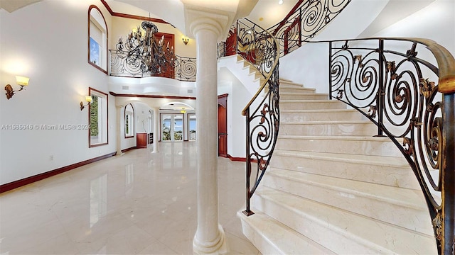 staircase with a towering ceiling, decorative columns, and tile floors