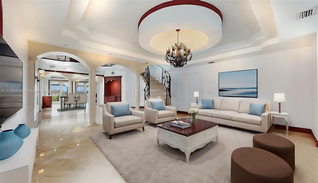 tiled living room featuring an inviting chandelier, decorative columns, and a raised ceiling