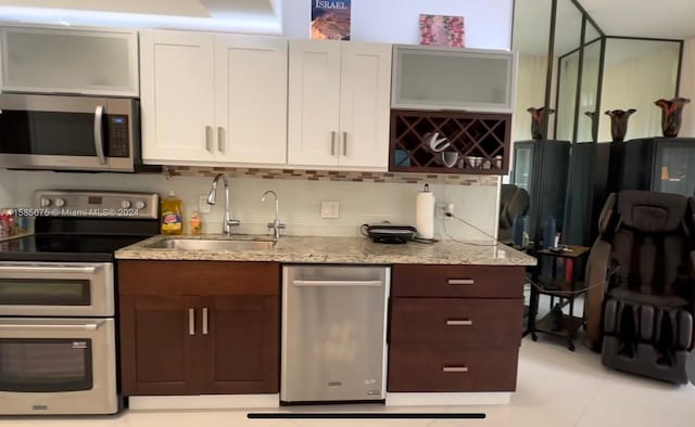 kitchen with light stone countertops, backsplash, stainless steel appliances, sink, and light tile floors