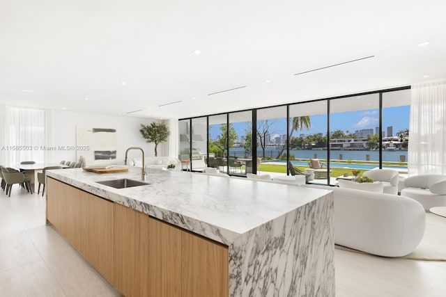 kitchen with light stone countertops, sink, a water view, and a center island with sink