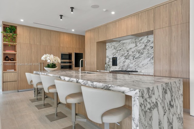 kitchen featuring a kitchen breakfast bar, stainless steel microwave, light stone countertops, and sink