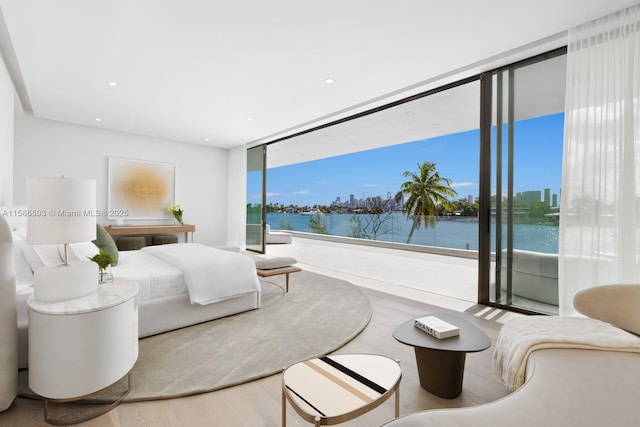 bedroom with wood-type flooring, a water view, floor to ceiling windows, and access to outside