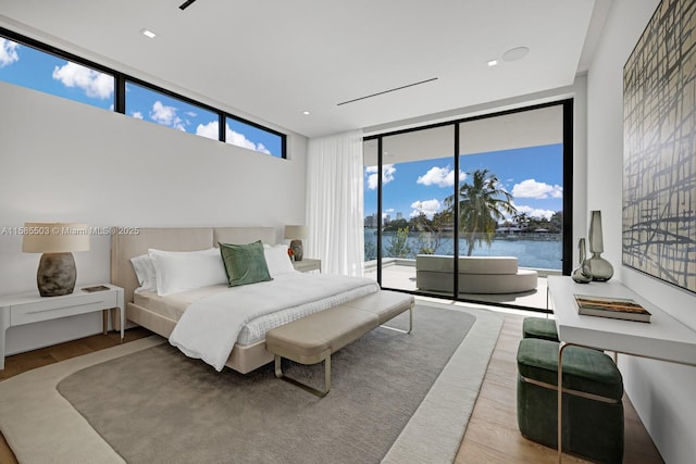 bedroom with expansive windows, hardwood / wood-style floors, a water view, and access to exterior