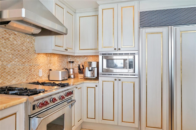 kitchen featuring white cabinets, wall chimney range hood, backsplash, and built in appliances