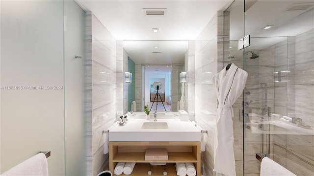 bathroom with a shower with shower door, vanity, and tile walls