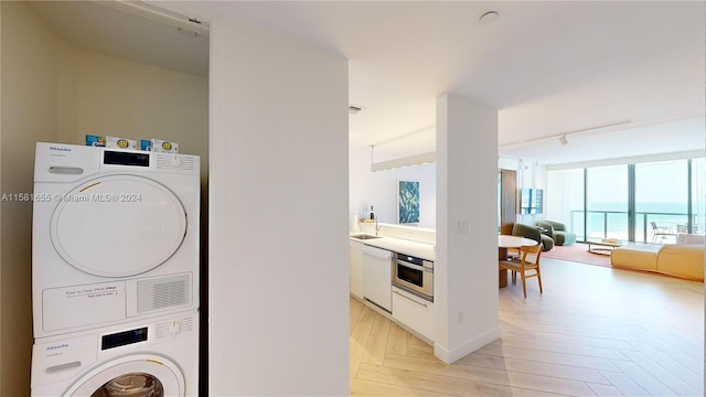 laundry room featuring a water view, stacked washer / dryer, track lighting, sink, and light parquet flooring