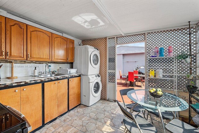 kitchen featuring tasteful backsplash, stacked washing maching and dryer, light tile flooring, range, and sink