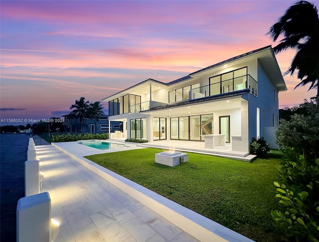 back house at dusk with a lawn, a balcony, and a patio