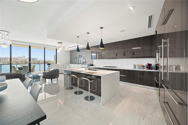 kitchen with a water view, sink, hanging light fixtures, an island with sink, and black cooktop