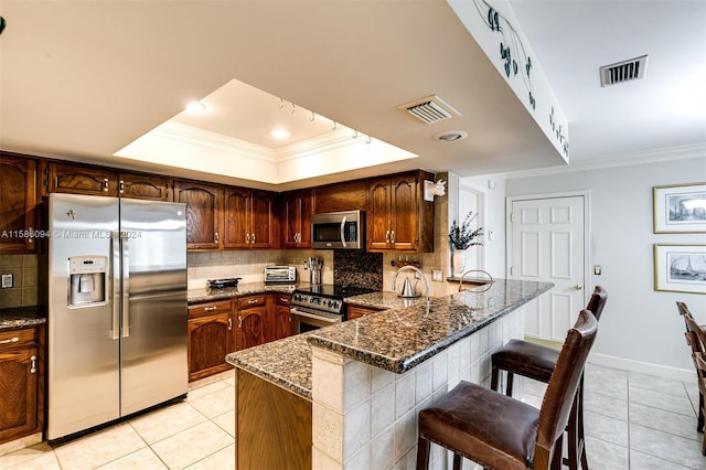 kitchen featuring decorative backsplash, stainless steel appliances, dark stone countertops, and a raised ceiling