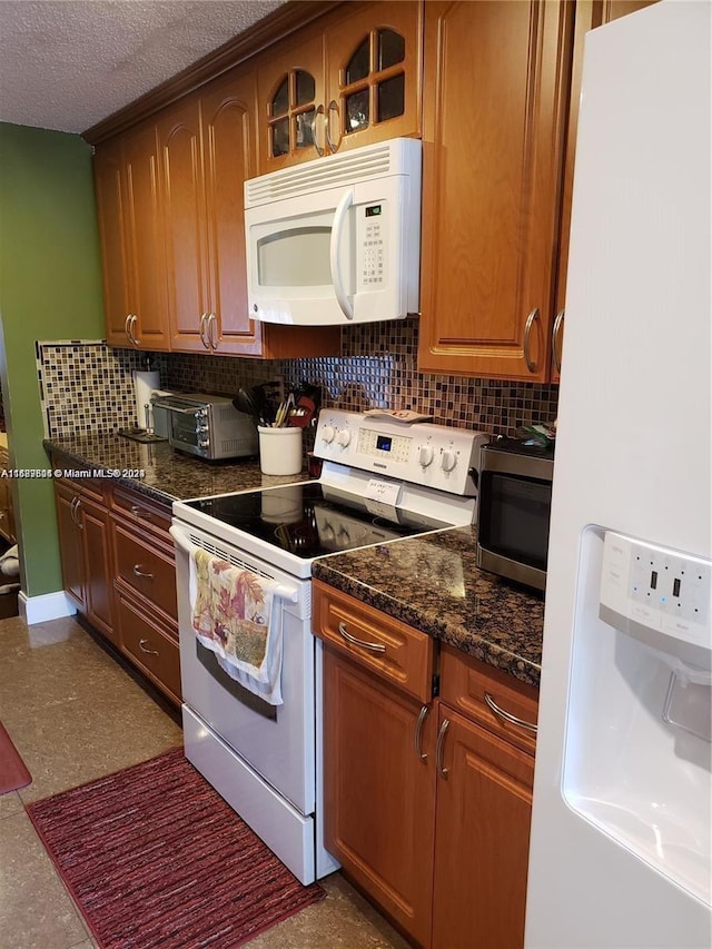 kitchen featuring a textured ceiling, dark stone countertops, decorative backsplash, and white appliances