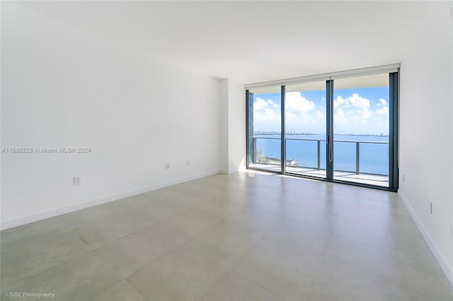 spare room with floor to ceiling windows, a water view, and tile floors