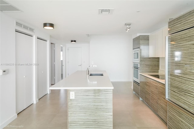 kitchen featuring stainless steel appliances, light tile floors, sink, a kitchen island with sink, and white cabinetry