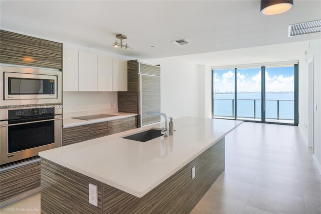 kitchen with appliances with stainless steel finishes, an island with sink, white cabinets, sink, and light tile flooring