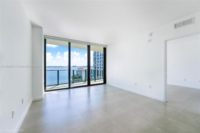 unfurnished room with tile flooring, floor to ceiling windows, and a water view