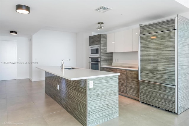 kitchen with an island with sink, sink, light tile floors, and appliances with stainless steel finishes