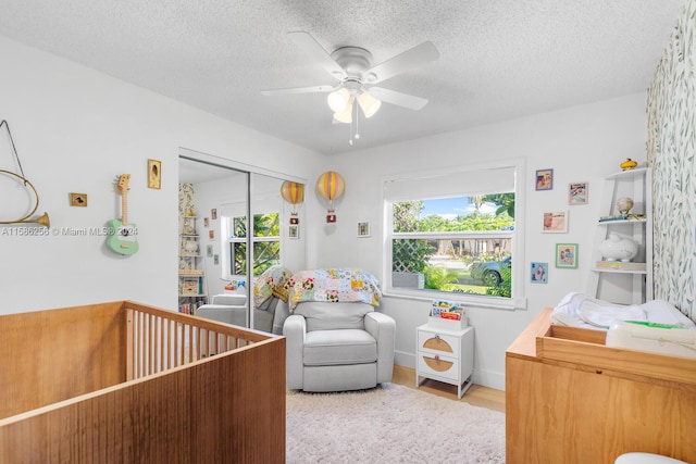 bedroom with light hardwood / wood-style floors, a textured ceiling, a crib, and multiple windows