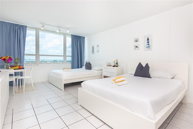 bedroom with track lighting, light tile flooring, and a water view