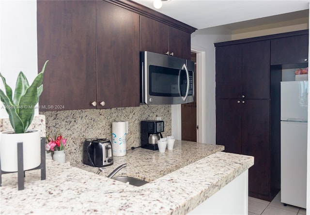 kitchen with white refrigerator, dark brown cabinets, backsplash, sink, and light tile floors