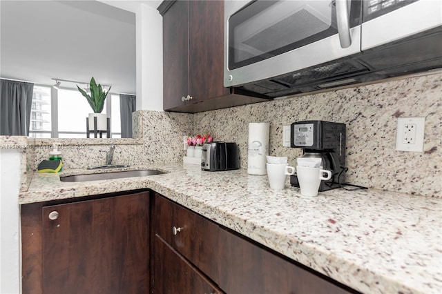 kitchen with sink, backsplash, dark brown cabinets, and light stone countertops