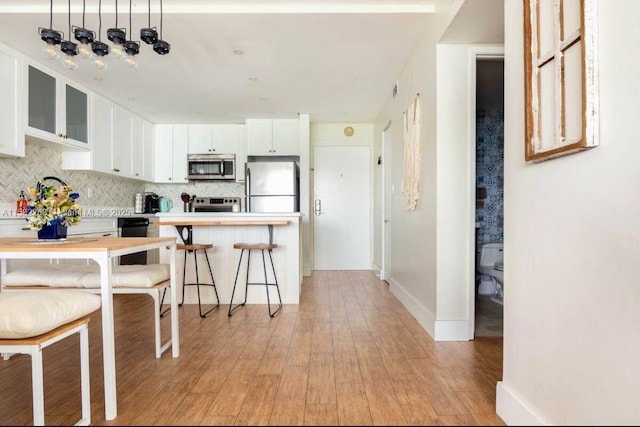 kitchen with white cabinets, backsplash, stainless steel appliances, and light hardwood / wood-style flooring