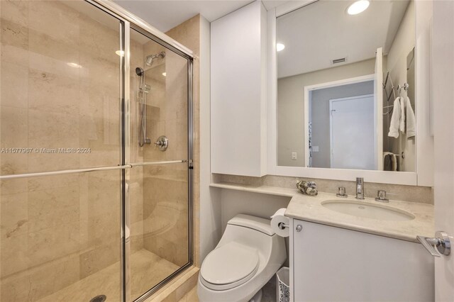 bathroom featuring a shower with shower door, vanity, and toilet