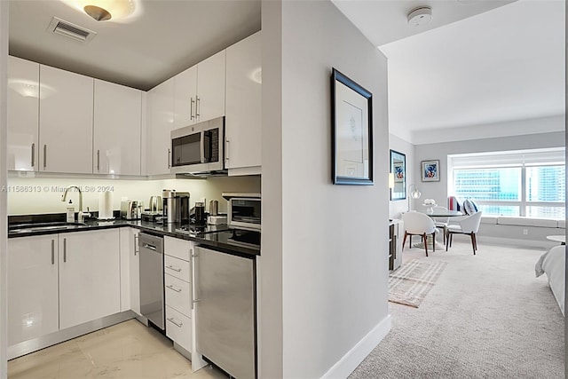 kitchen featuring sink, stainless steel appliances, light carpet, and white cabinetry