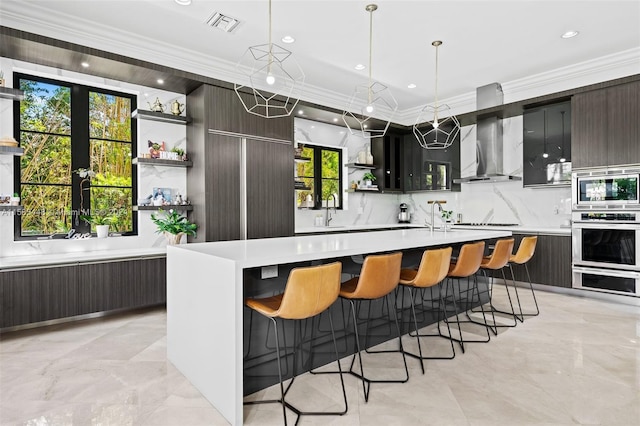 kitchen featuring wall chimney range hood, an island with sink, and a wealth of natural light