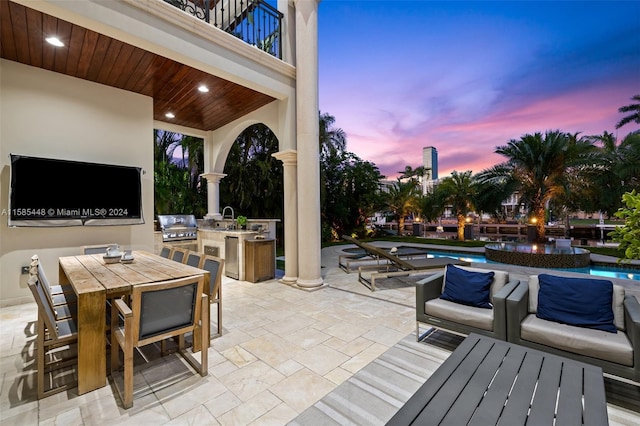 patio terrace at dusk with a balcony, sink, and area for grilling