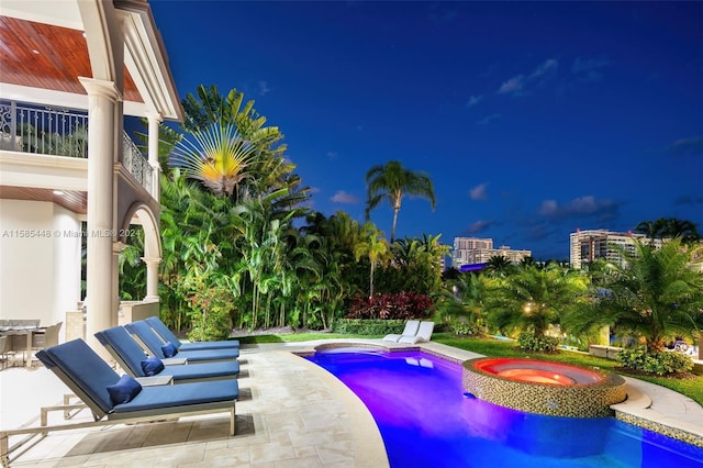 pool at twilight with a patio and an in ground hot tub