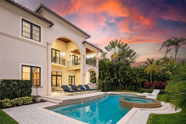 pool at dusk featuring a patio area and an in ground hot tub