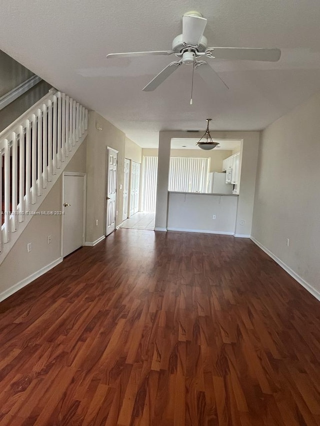 unfurnished living room with stairway, wood finished floors, a ceiling fan, and baseboards