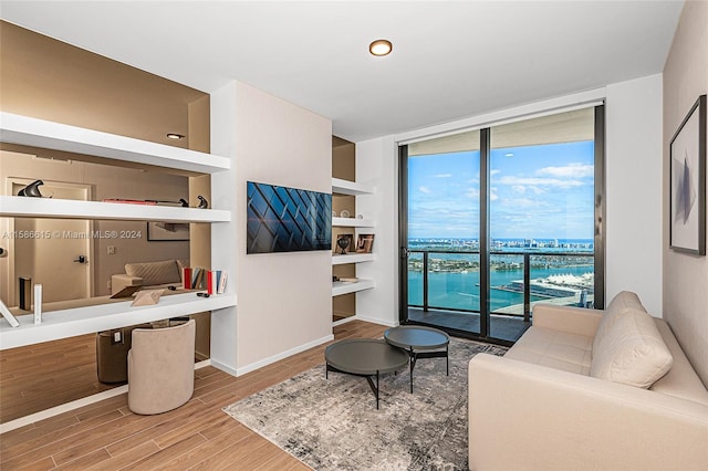 living room with built in desk, wood-type flooring, a water view, and expansive windows