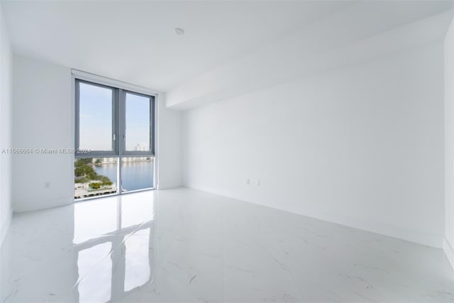 empty room with tile floors, a water view, and a wall of windows