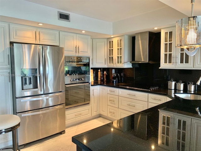 kitchen with dark stone counters, hanging light fixtures, tasteful backsplash, wall chimney exhaust hood, and appliances with stainless steel finishes