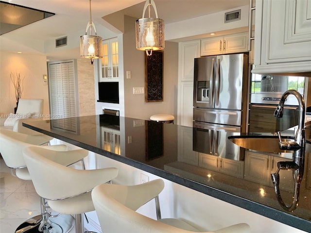 kitchen featuring stainless steel fridge, hanging light fixtures, cream cabinetry, a breakfast bar, and sink