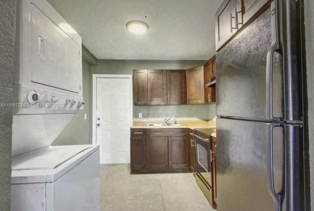 kitchen featuring electric range, stacked washer / dryer, black refrigerator, sink, and light tile floors