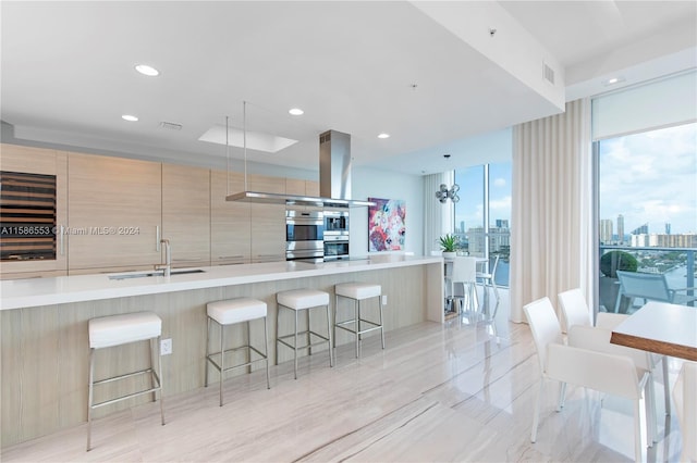 kitchen featuring a kitchen breakfast bar, sink, double oven, and island exhaust hood