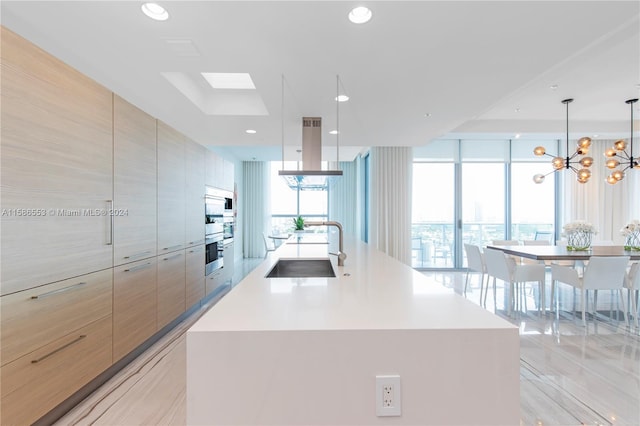 kitchen featuring a skylight, a notable chandelier, island range hood, an island with sink, and a wall of windows