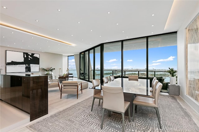 dining space featuring a water view, plenty of natural light, light wood-type flooring, and a wall of windows