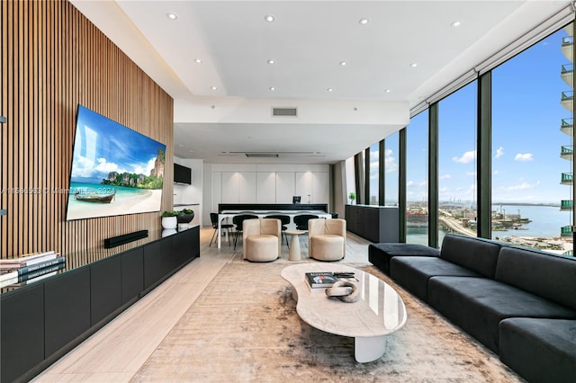 living room featuring a water view, light wood-type flooring, and a wall of windows