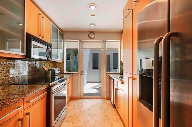 kitchen with appliances with stainless steel finishes, a healthy amount of sunlight, backsplash, and dark stone countertops