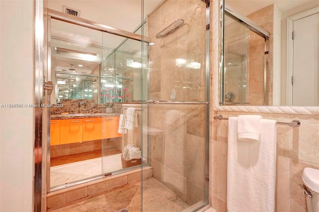 bathroom featuring a shower with door, vanity, toilet, and tile walls