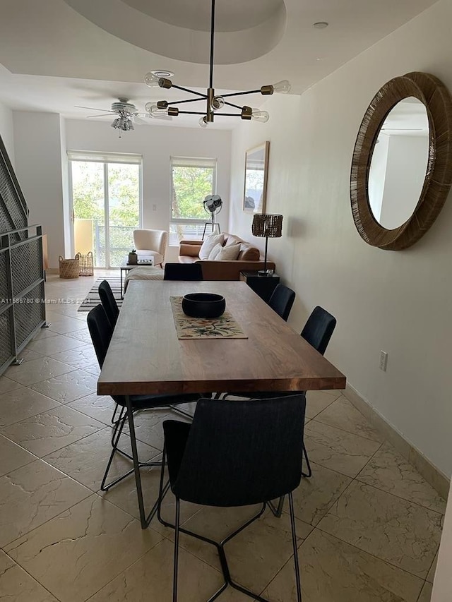 tiled dining area with ceiling fan with notable chandelier and a raised ceiling