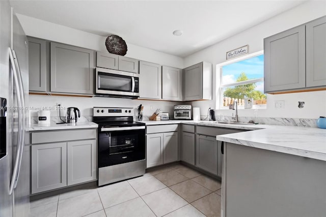 kitchen featuring light stone countertops, stainless steel appliances, sink, light tile patterned flooring, and gray cabinets